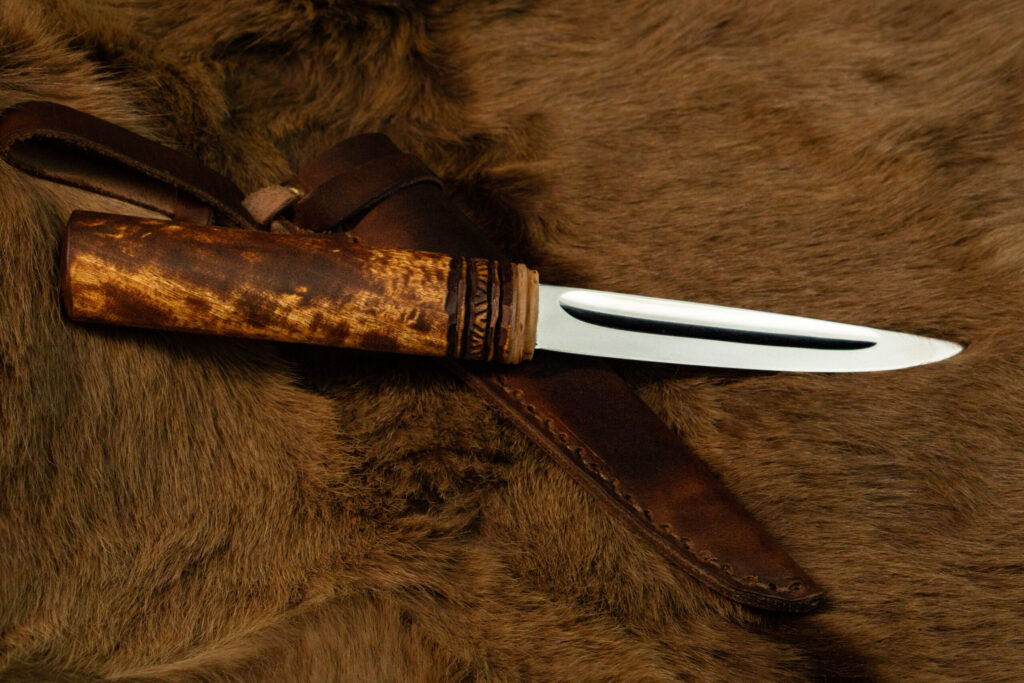 Yakut knife showing the flat side with its wide hollow (dol), beside a leather sheath
